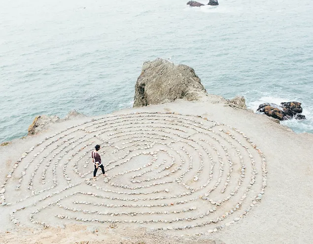 Labyrinthe de pierres tracé sur une falaise au bord de l'océan, une personne cheminant vers son centre