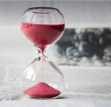 Sablier au sable rose posé sur un journal, évoquant le temps qui s'écoule